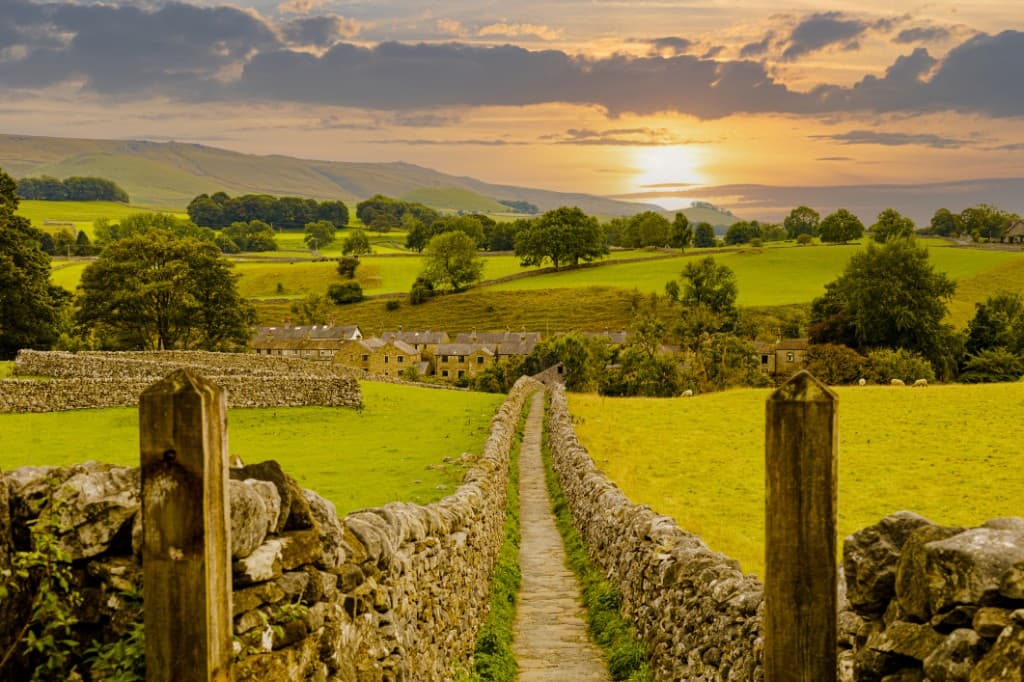 Stone-walled path leading toward a village at sunset
